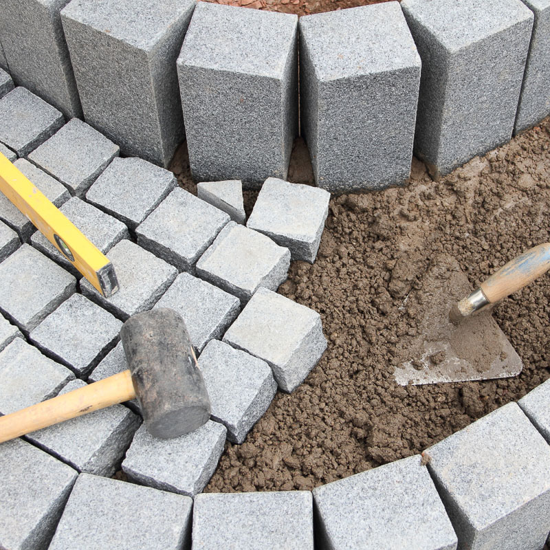 Truelle, niveau et marteau sur pavé granit