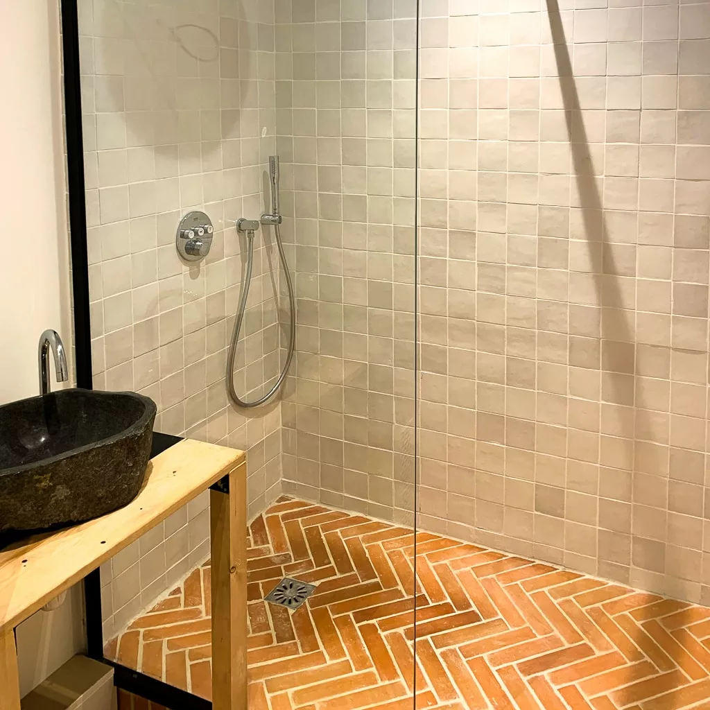 Salle de bain originale avec une vasque noire et des briques sur le sol de la douche